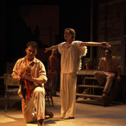 A young man holds a rooster while a girl in angel wings stands nearby with outstretched arms