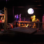 Groups of people on a large old-looking industrial stage structure pose on various vignettes