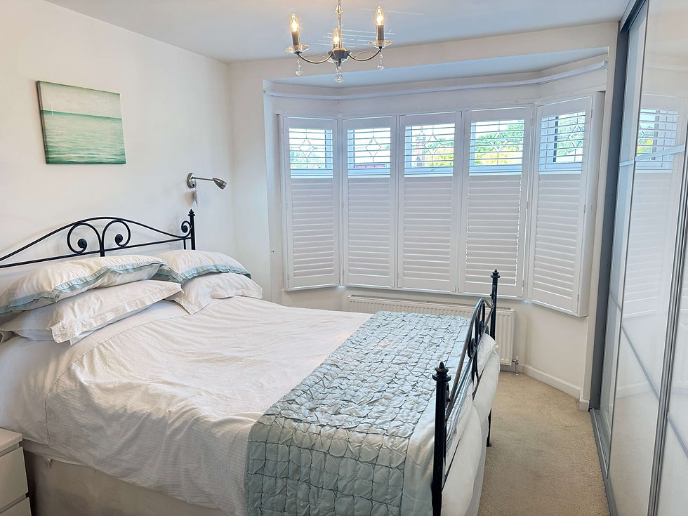 Full height hardwood bay window shutters fitted in an Bury St Edmunds bedroom by Miavalentina Interiors showing privacy split and 63mm Paulownia louvres