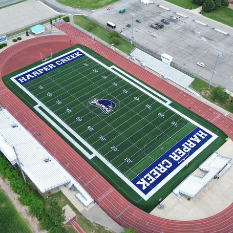A view of the high school football field, featuring green turf, goalposts, and surrounding bleachers under a clear sky.