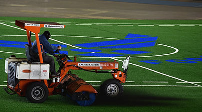 A man cleans a synthetic turf field with a machine, highlighting the importance of turf maintenance services.