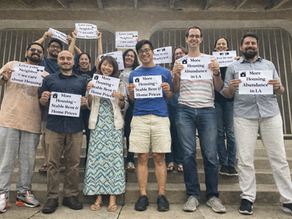 Members of The Faith & Housing Coalition celebrate by holding up signs that say "More Housing=Stable Rent & Home Prices" and "Love your Neighbor=we care about housing" "More Housing Abundance in LA" "Yes in our Backyard"