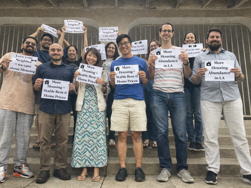 Members of The Faith & Housing Coalition celebrate by holding up signs that say "More Housing=Stable Rent & Home Prices" and "Love your Neighbor=we care about housing" "More Housing Abundance in LA" "Yes in our Backyard"