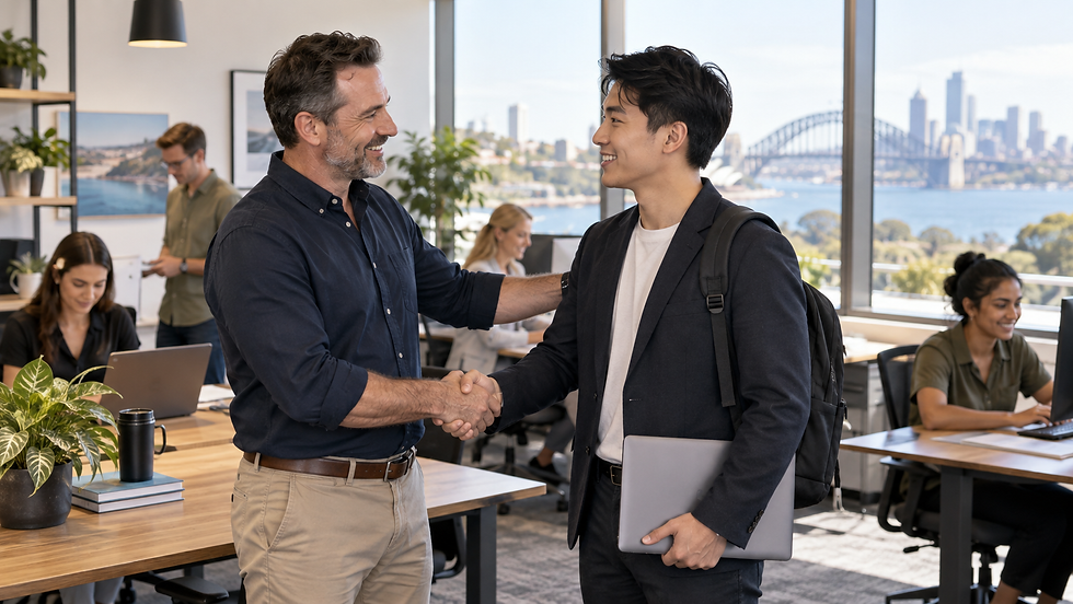 A small business owner welcoming an overseas specialist to an active workplace with local colleagues working in the background in Australia