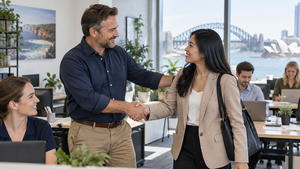 A small business owner welcoming an overseas specialist to an active workplace with local colleagues working in the background in Australia