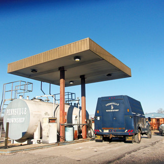 Angled view of two aging aboveground fuel tanks labeled 'Pennsville Township,' with visible wear under an older fueling canopy, as a Pennsville Water Department service truck refuels nearby.