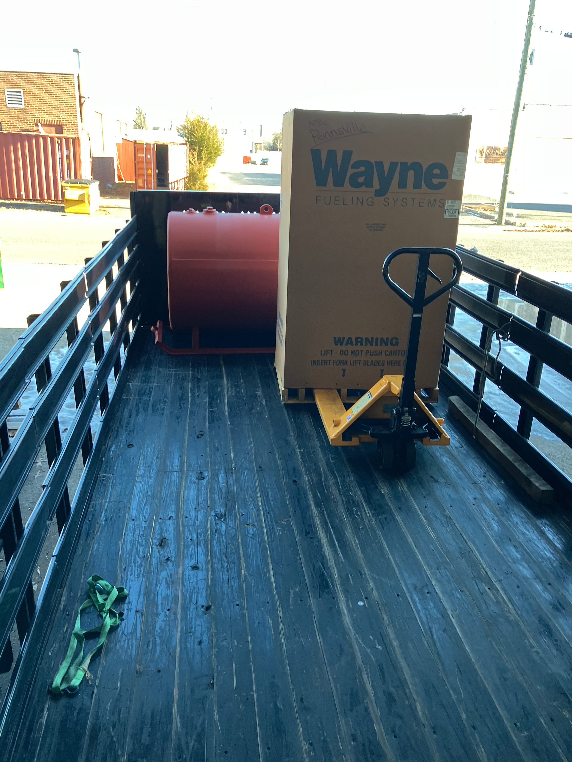Wayne Fueling Systems dispenser and red storage tank secured on a flatbed for project delivery.