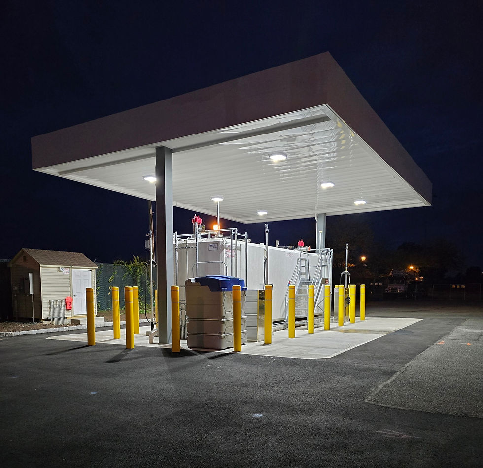 An illuminated outdoor installation site featuring essential equipment for fuel distribution under a protective canopy. The setup is secured with yellow safety bollards, ensuring safe and efficient operations even at night.