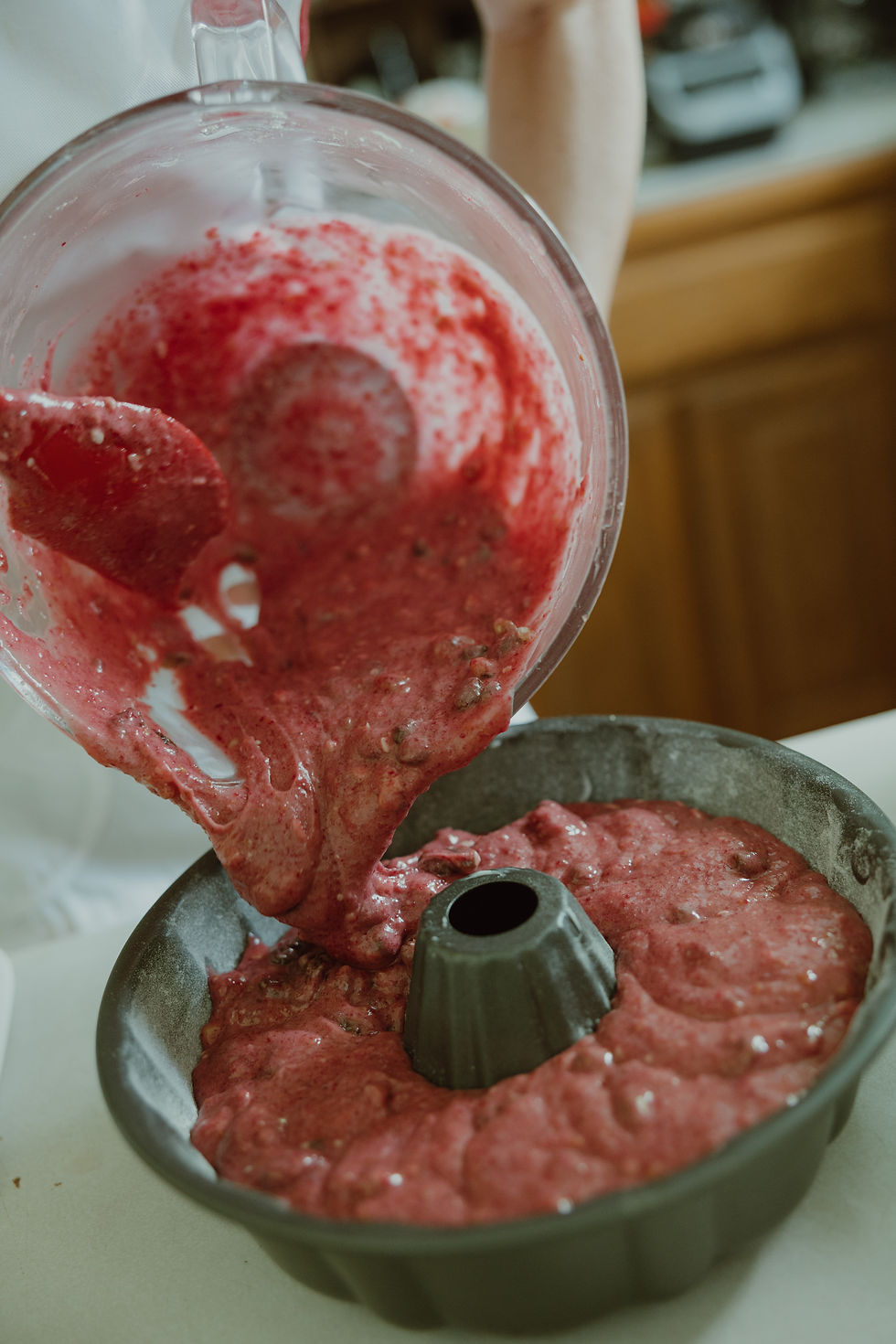A bowl of pink cake batter is poured into a bundt pan