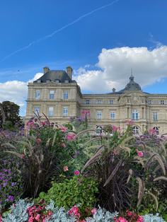 Luxembourg Palace stands majestically behind colorful garden blooms and blue sky.