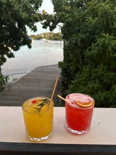 Refreshing yellow and red cocktails on a railing by a scenic river.