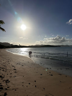 Two people walk on a serene beach as sun sets over the ocean.