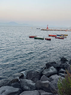 Calm sea with colorful boats near a red lighthouse and rocks.