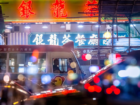 Double exposure night shot of a minibus standing near a shop with neon sign