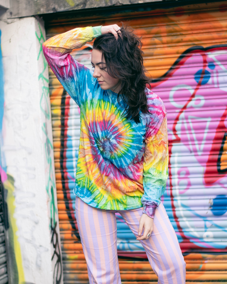 A young woman with dark hair and psychedelic tie dye top, urban hipster photoshoot with graffiti in the background