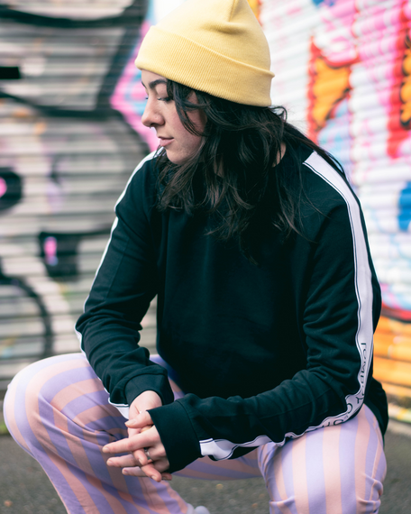 A young woman with dark hair and yellow beanie hat, urban hipster photoshoot with graffiti in the background, Brighton model
