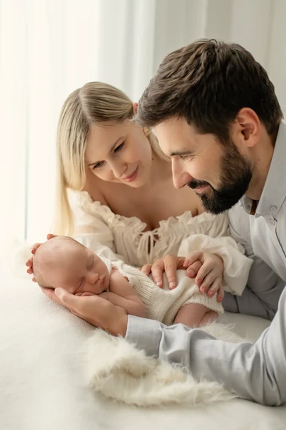 Dziecko w dłoniach taty i przytulona mama na sesji noworodkowej