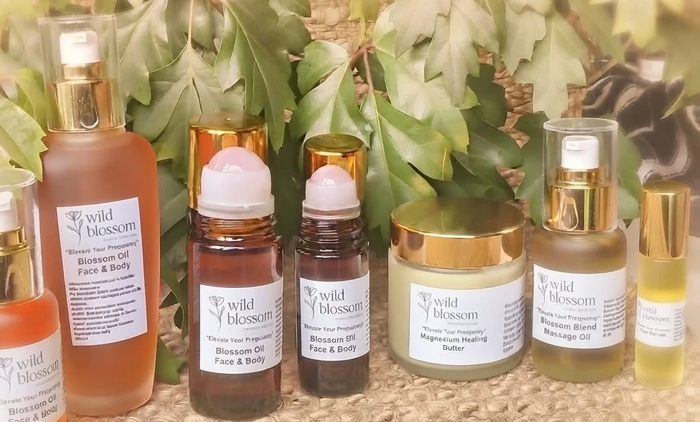 Packshot photography displaying a collection of Wild Blossom branded skincare products, including glass pump bottles, rollerballs, and a jar, arranged on a textured surface with green foliage behind them. The lighting creates a serene, natural, and organic atmosphere.