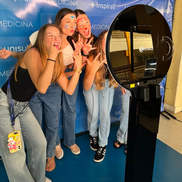 Grupo de pessoas se divertindo em frente ao Totem de Fotos da Festalize com fundo de lona personalizado de marca em evento institucional.