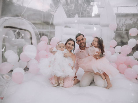 Ensaio fotográfico de família (mãe, pai e filha bebê) dentro da Bolha Mágica da Festalize decorada com balões claros, gerando memórias.