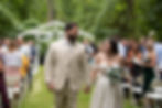 Bride and groom smiling as they walk hand-in-hand down the aisle just after their outdoor wedding ceremony, surrounded by cheering guests in a forested venue.
