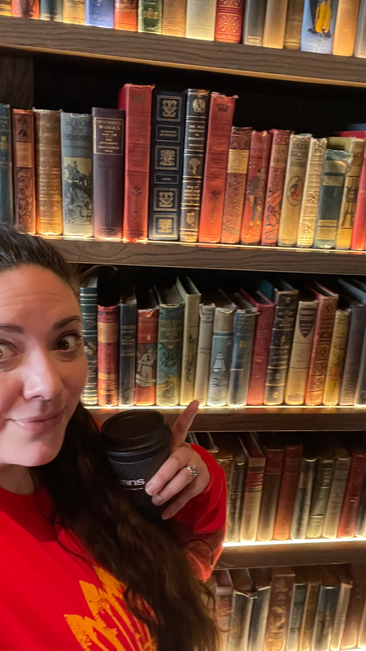 woman stands in front of a bookshelf, pointing at the old hardback books