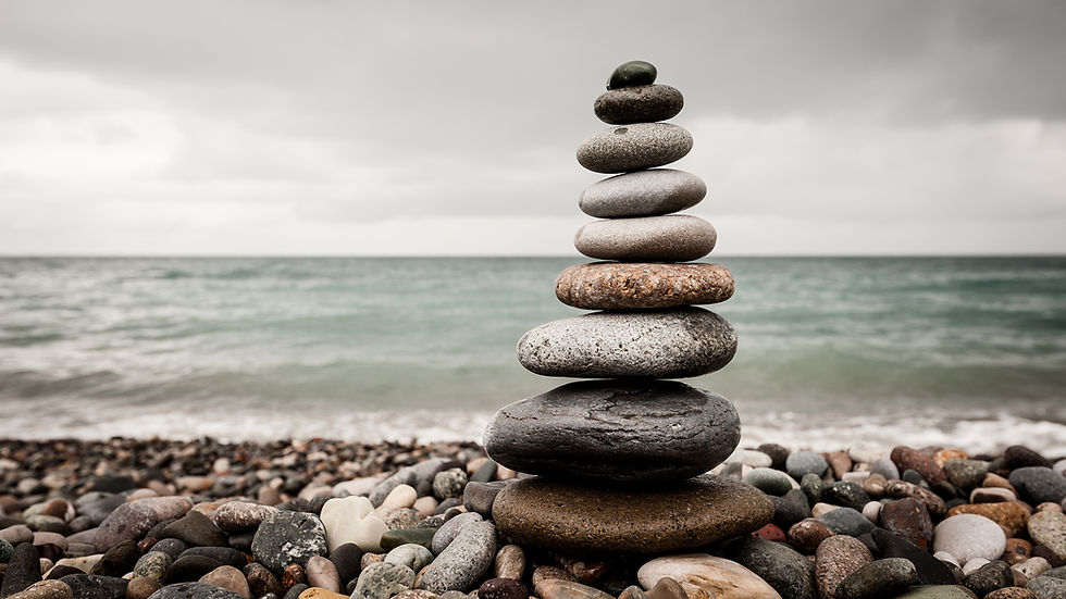 Stack of smooth stones balances on a pebbly beach with gray clouds and a calm sea in the background, evoking a serene mood.