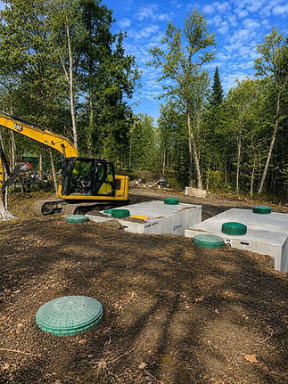 Excavator backfilling around multiple septic tanks during installation on a residential construction site