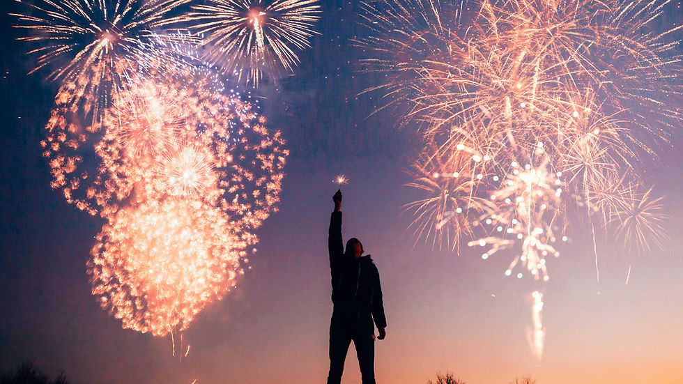 Silhouette of a person holding a sparkler against a twilight sky, with vibrant fireworks exploding overhead, creating a festive mood.