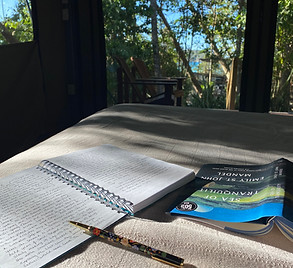 A book and a notebook and pen lying open on a bed, beautfil woods in the background