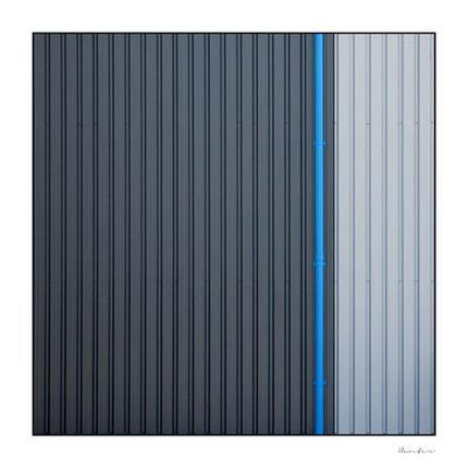 Abstract architectural detail of vertical ribbed metal siding in dark charcoal and light grey, split by a thin bright blue drainpipe.