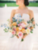 Bride looking over her shoulder in a modern strapless wedding gown with a dramatic bow, holding a spring bouquet at a Korean - Mexican Multicultural Wedding at The Jewel Box at Forest Park in downtown St. Louis, MO.