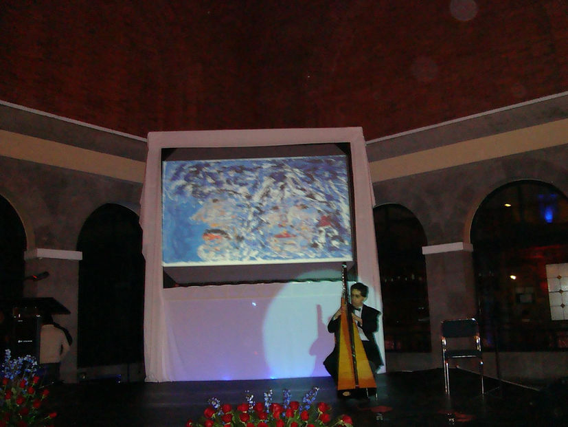 Pantalla pasando las obras y músico tocando Arpa durante el evento. Obra Pareja de Carlos