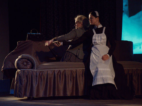A maid in an apron is sitting next to Hedda Gabler on stage - scene from "Hedda Gabler' play staged by Diana Stein.