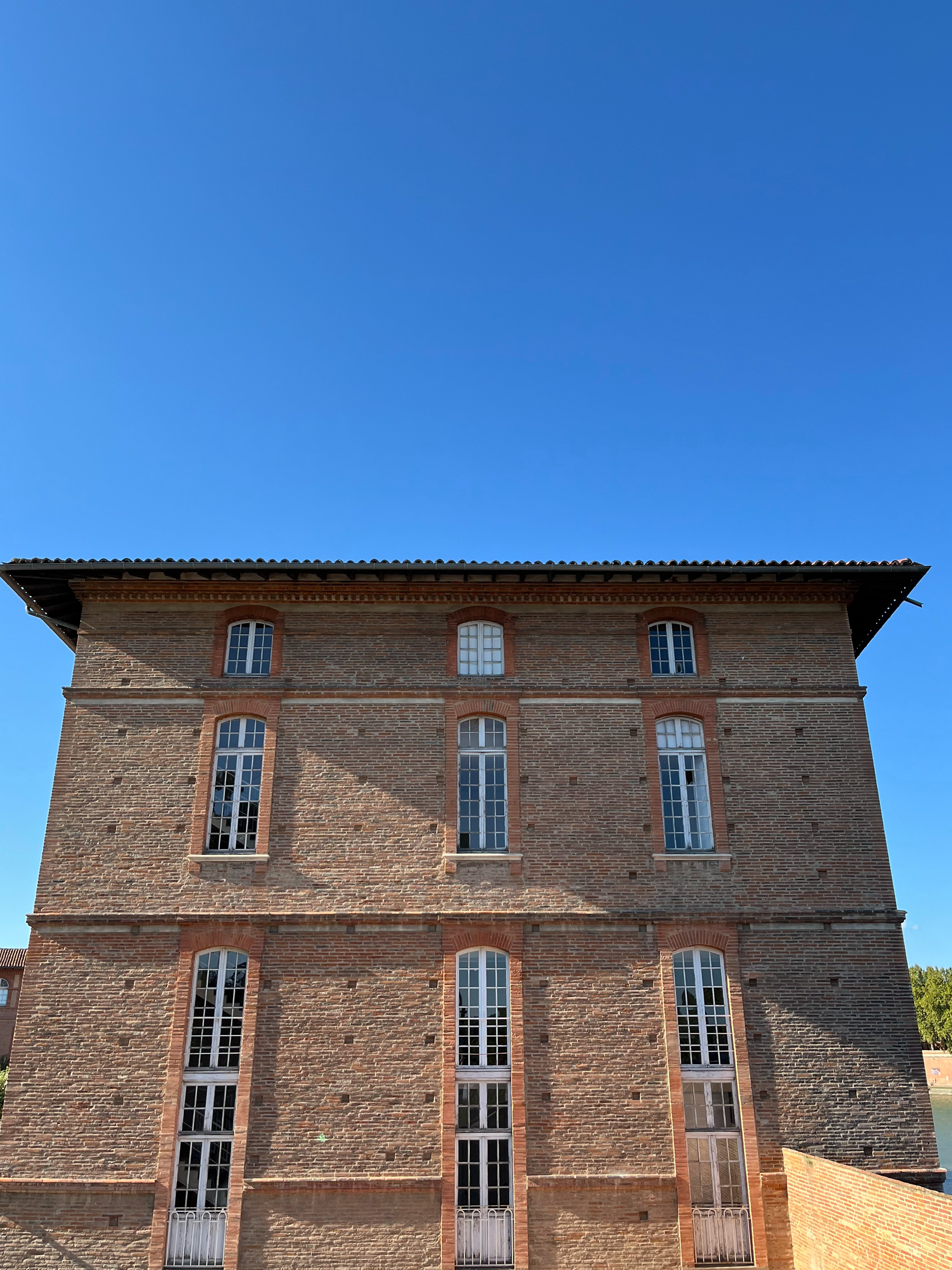 Façade à l'architecture typique de Toulouse avec grandes fenêtres d'époque.
