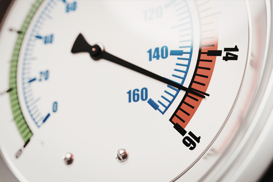 Close-up of a pressure gauge with a black needle pointing to red and blue sections. Numbers 0-160 in black and blue, indicating high pressure.