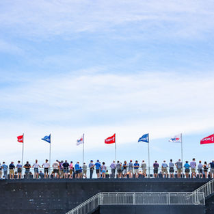 Guests at the U.S. Open in a line with U.S. Open flags under a blue sky