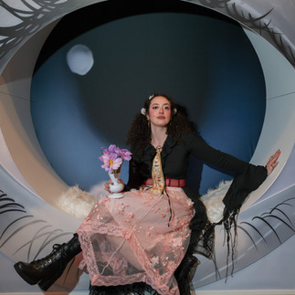 Girl in surrealism themed outfit sitting in seat that looks like a massive eye