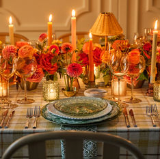 Candlelit table setting with plaid tablecloth, pink florals, and green and gray plates