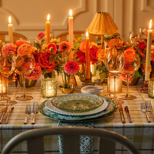 Candlelit table setting with plaid tablecloth, pink florals, and green and gray plates