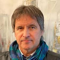 Hier siehr man ein Porträtfoto von Mag. Norbert Wiesflecker aus Villach. Der Hintergrund ist Beige und er trägt einen türkiesen Schal.