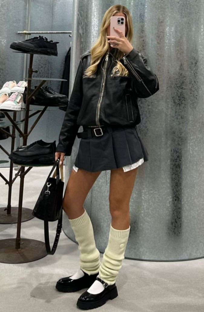 a women taking a mirror selfie wearing leather jacket and mini skirt and leg warmers