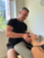 Chiropractor in black shirt giving a neck adjustment to a relaxed woman on a treatment table in a bright, treatment room at Peridot Wellness.