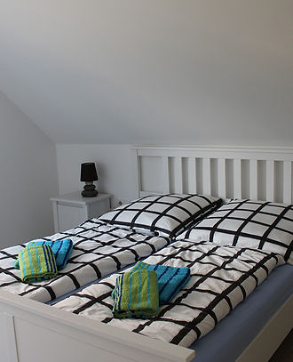 Zu sehen ist hier eines der Schlafzimmer. Abgebildet ist ein frisch gemachtes Bett und auf diesem Bett liegen Handtücher für die Gäste bereit.