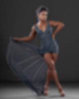 Woman in a sparkly blue dress poses confidently, holding the hem. Dark background, elegant mood, clear heels, hair tied up.