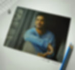 Drawing of a man in a blue shirt, leaning on a window, with a reflective expression. Two pencils lie beside the artwork.