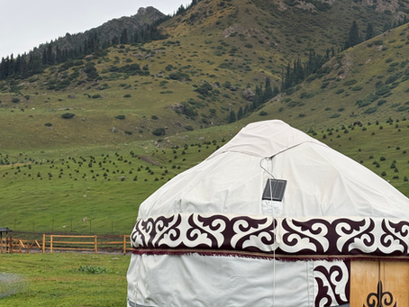 Yurt in a grassy field with grassy hills in the background