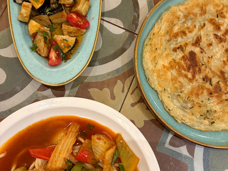 Noodle dish, eggplant and tomato salad, and fried bred in dishes on a tile patterned table
