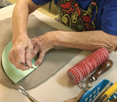Senior's hands, hand building with clay during pottery class to make a dessert cup, using texture tools