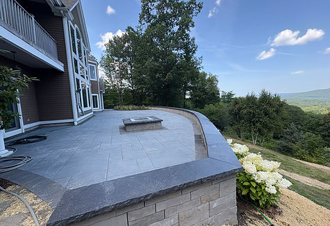 A large modern Techo-Bloc patio with tall retaining wall, fire pit, lighting and plantings in Brattleboro VT